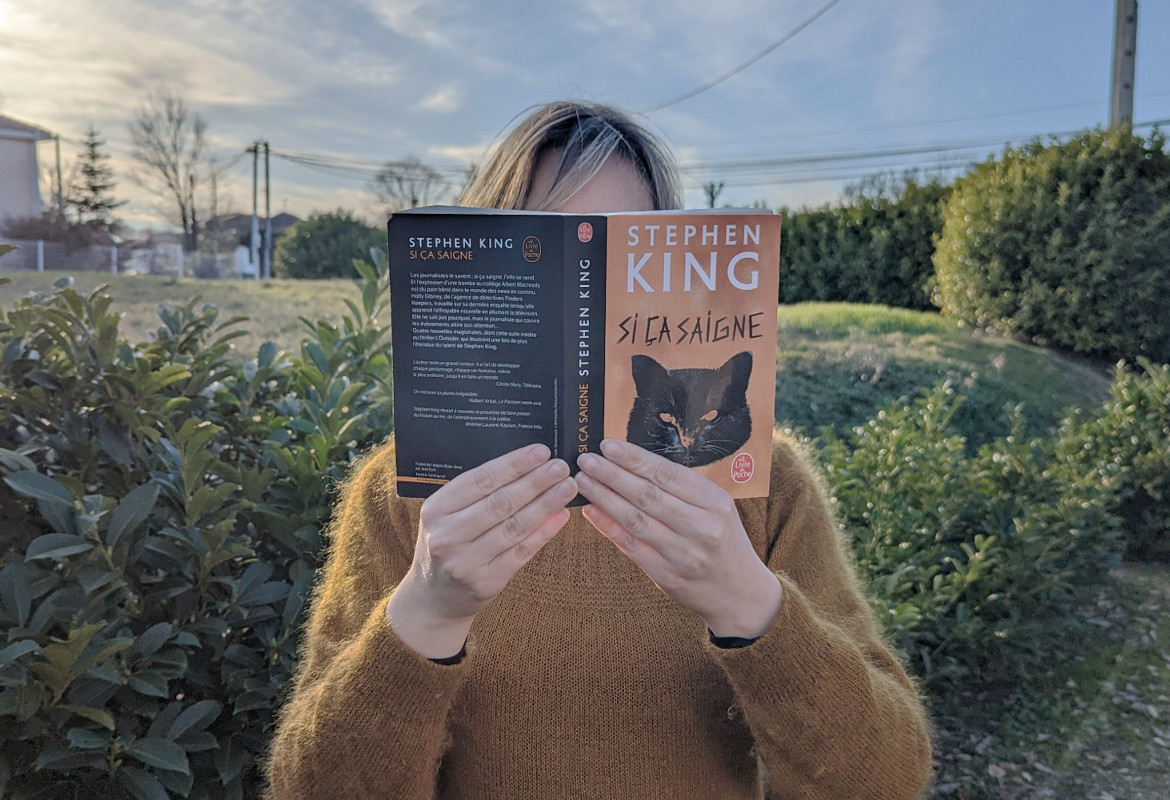 Femme tenanit le livre Si ça saigne de Stephen King devant son visage